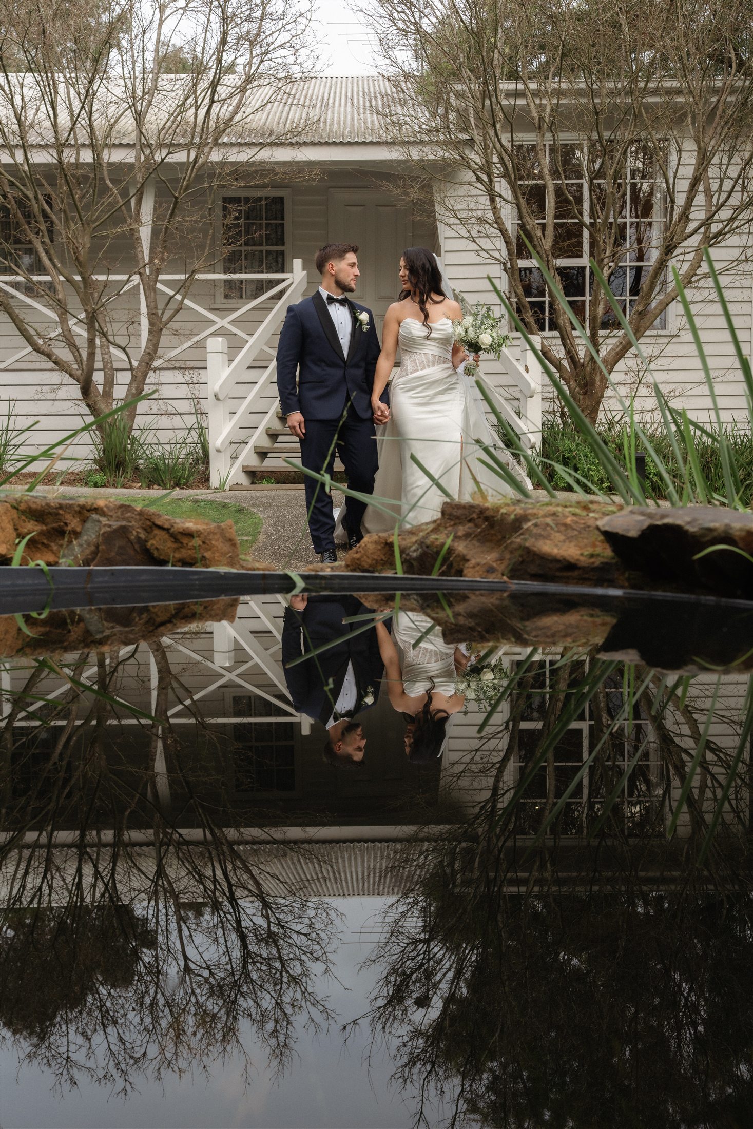 Afonso and Agnes reflected in a pond beside a white cottage